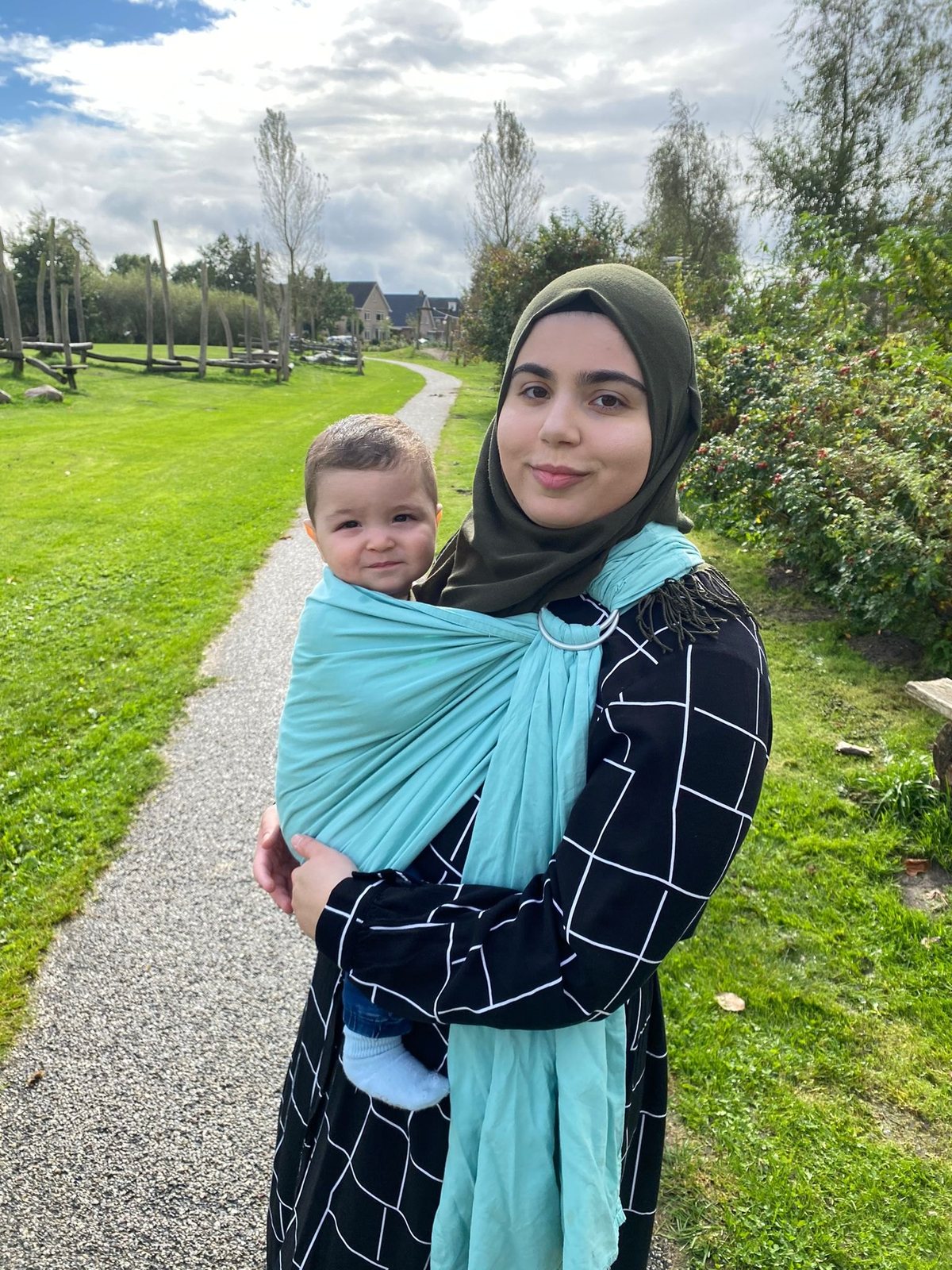 Feride draagt haar baby buiten in een turquoise ringsling
