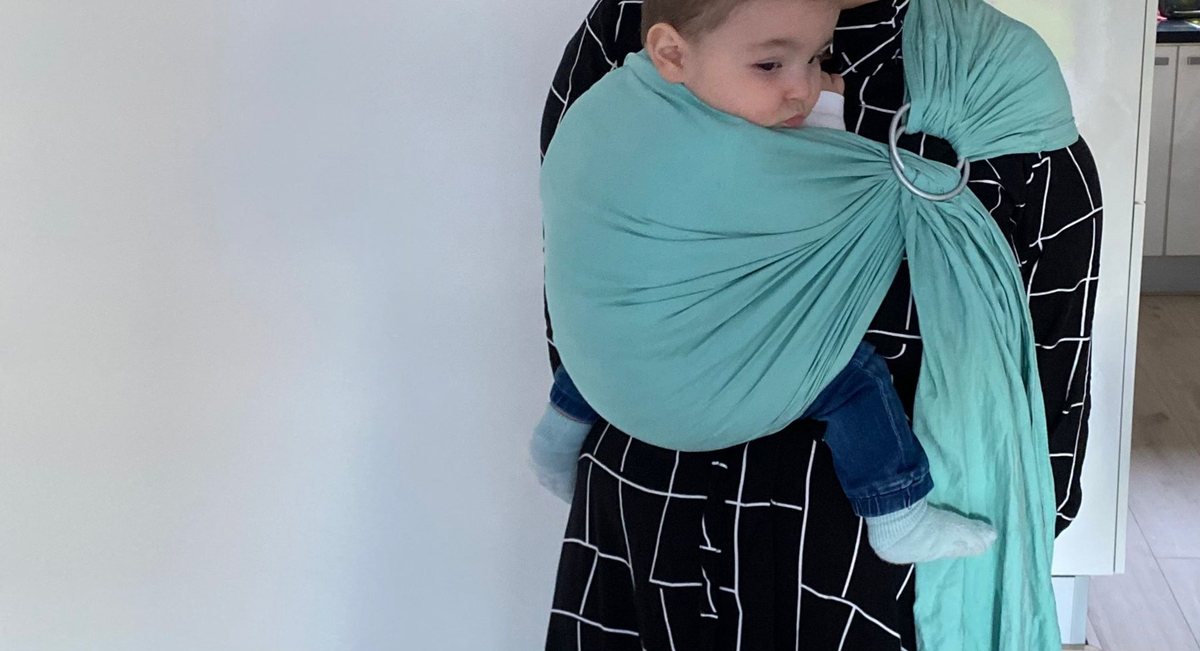 Een kind wordt binnen gedragen in een turquoise ringsling