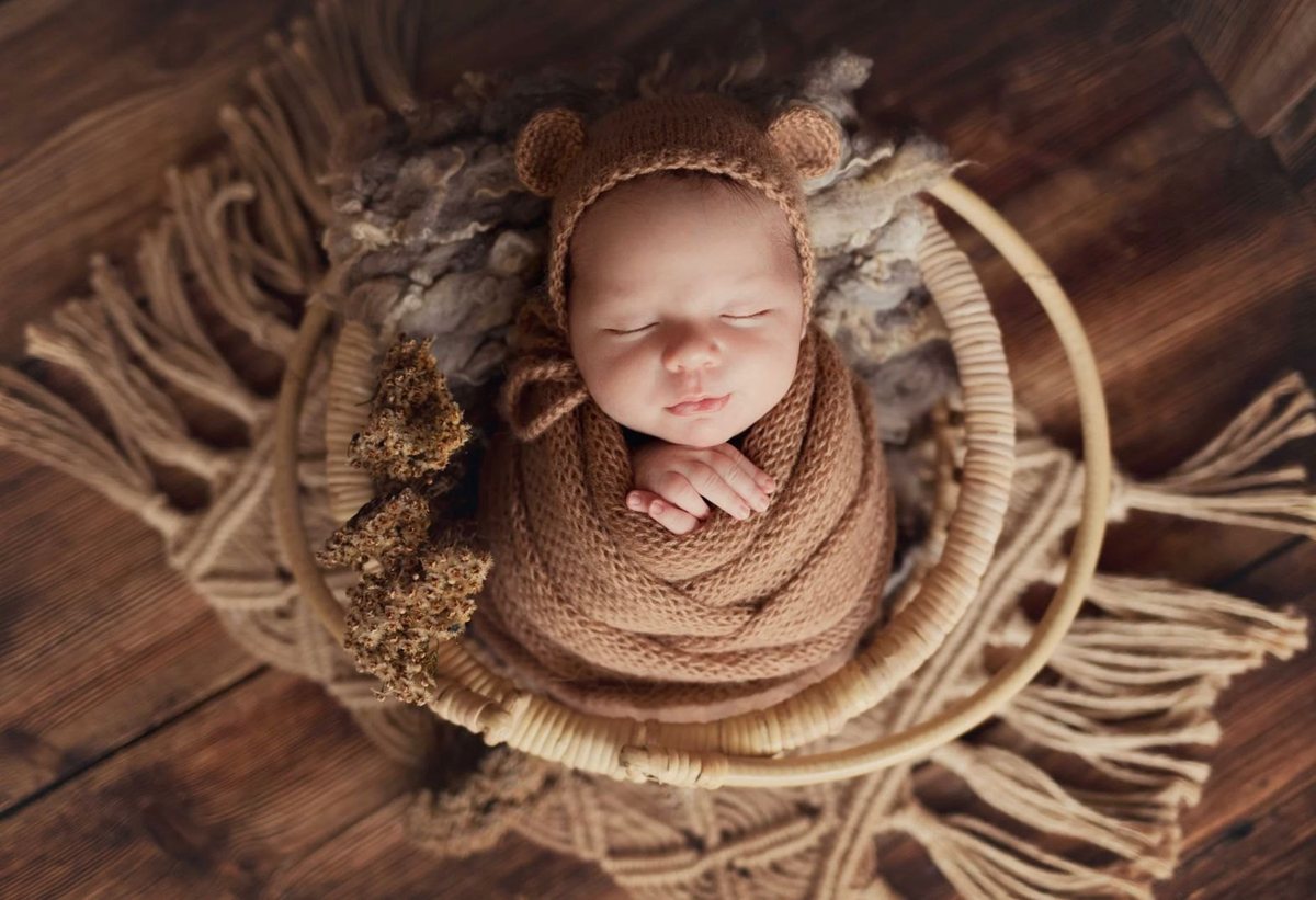 Een pasgeboren baby slaapt ingebakerd in een gebreide doek op een houten ondergrond